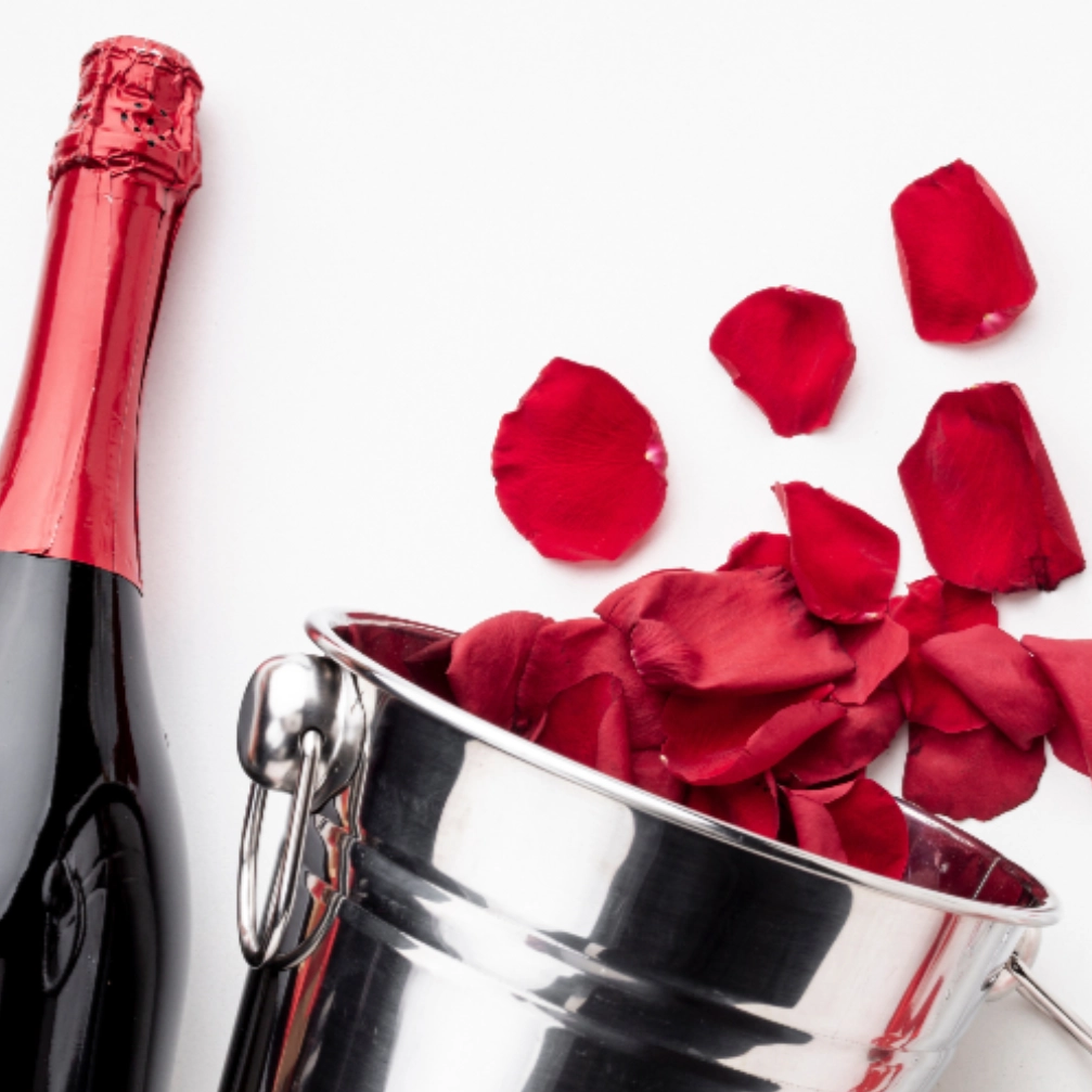Saut à champagne rempli de pétales de rose rouge avec coupe et bouteille de champagne.